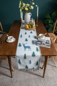 Detail of pine tree and blue deer pattern on knitted table runner with colorful bead tassels