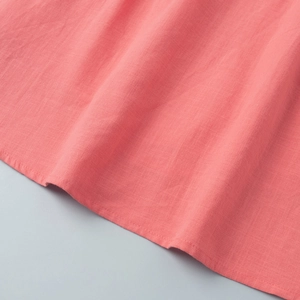Macro detail of coral pink cotton fabric texture and fine hem stitching on the skirt