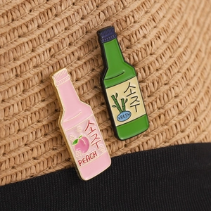 Detail of peach and soju bottle enamel pins attached to a straw hat band