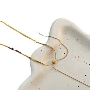 Golden snake chain necklace with adjustable sliding bead buckle on white ceramic tray