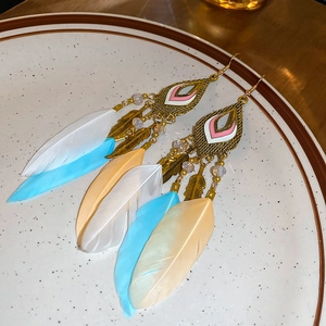 Macro detail of Bohemian feather drop earrings with beads and gold metal leaf accents
