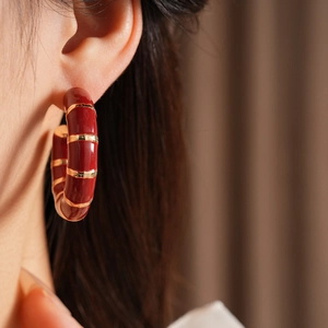 Close-up of a vintage burgundy enamel C-shaped hoop earring with gold stripes on model