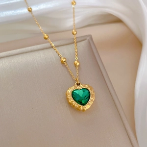 Macro shot of green heart pendant necklace on gold chain over soft fabric