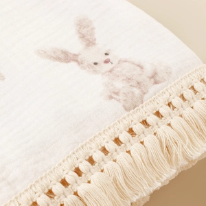 Close-up of double-layer cotton muslin baby blanket with pink rabbit prints and tassels