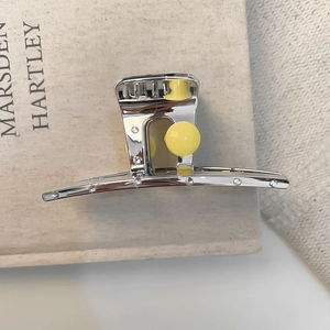 Elegant silver metal hair claw with yellow pearl and crystals on a minimalist background