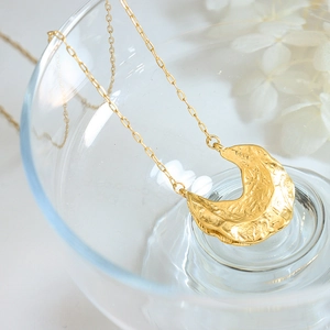 Gold moon pendant necklace with irregular hammered texture on transparent glass cup