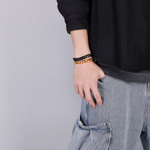 Detail of stacked black and gold stainless steel Cuban link chains on a male wrist
