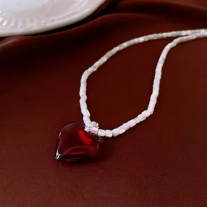 Elegant cat eye beaded necklace with a vibrant red heart pendant on silk background