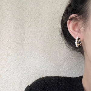 Détail de boucles d'oreilles créoles avec chaîne entrelacée, perles et un zircon central