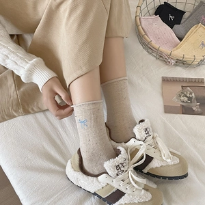 Detailed knit texture of mid-calf socks featuring blue bow embroidery and rolled cuffs