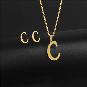 Golden letter C pendant necklace and earrings set on a black minimalist pedestal