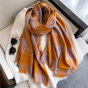 Detail of soft orange and pink plaid scarf with fringe tassels on a white sweater