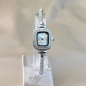 Macro shot of silver square watch dial with quartz movement and rhinestone-set band