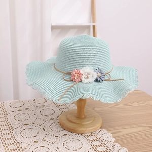 Détail d'un chapeau de paille vert menthe avec fleurs en tissu 3D et perles décoratives