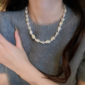 Close-up of irregular white baroque pearl necklace worn on a grey sweater