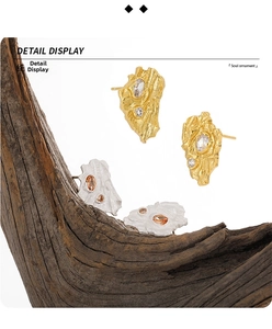 Detail view of irregular textured gold and silver earrings with zircon on wood base