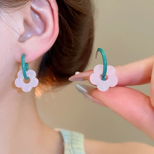 Detail of pink resin flower earrings with green hooks shown in a hand-held close-up shot