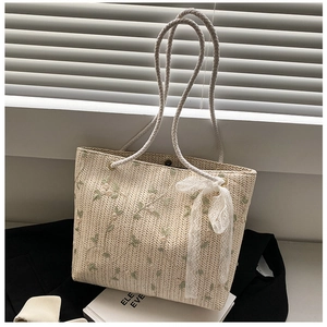 Detailed close-up of straw tote bag with lace bow decoration and floral embroidery
