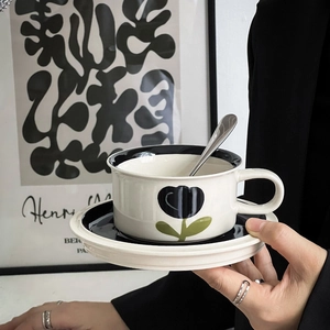 Detail of vintage hand-painted ceramic coffee cup with black floral patterns and gold spoon