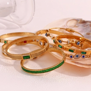 Detail of 18K gold-plated bracelets with green zircon and evil eye on a shell background