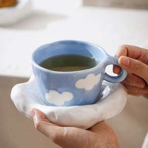 Close-up of handmade blue ceramic mug with white clouds and irregular cloud saucer