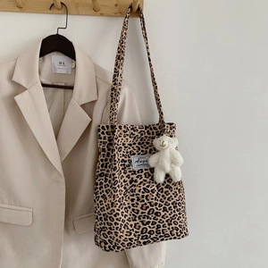 Detail of leopard print canvas tote with plush bear charm hanging on a wooden hook
