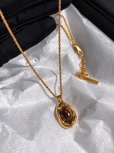 Detail of gold-plated rope chain with oval brown tiger eye pendant held in hand