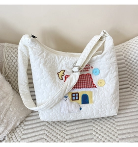 Detail of white quilted tote bag featuring house and animal embroidery with zipper closure