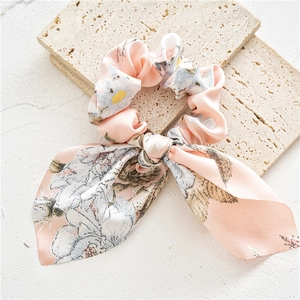 Detail of pink floral satin scrunchie with elegant ribbons on a marble surface