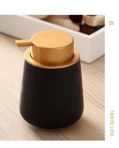 Detail of matte black ceramic soap dispenser with a gold pump on a wooden surface