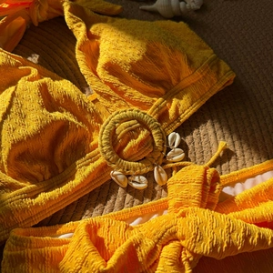 Detail of yellow seersucker bikini top featuring straw ring and natural sea shell accents