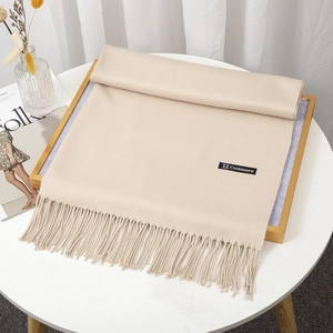Elegant beige cashmere scarf with tassels and black label on a minimalist setup