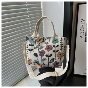 Close-up of beige canvas tote bag featuring colorful floral patterns and adjustable strap