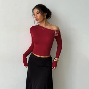 Detail of burgundy off-shoulder top with 3D rose accent and asymmetric sleeve design