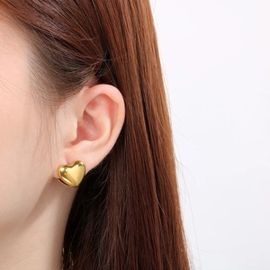 Polished gold heart stud earrings in titanium steel worn by a model in a profile view