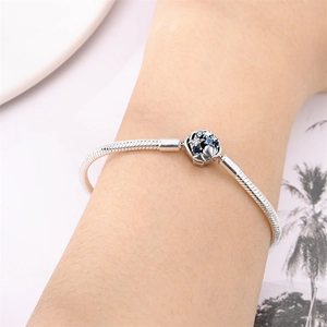Close-up of a silver snake chain bracelet featuring a blue gemstone flower bead charm