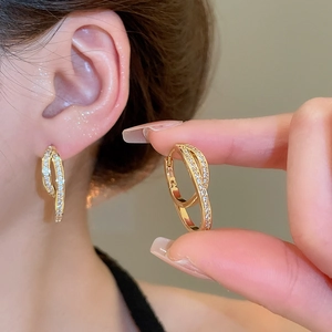 Detail of 18k gold plated U-shaped earrings with cross-twisted design and inlaid zircons