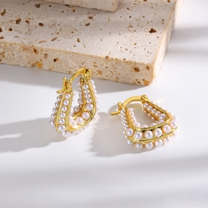 Détail des boucles d'oreilles dorées en U avec incrustations de perles sur surface en pierre