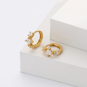 Detail view of gold hoop earrings with clear square and round zircons on stone stand