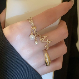 Detailed view of layered gold rings with pearls, zircons, and bow charm on model hand