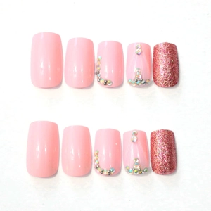 Detailed view of pink press-on nails with glitter accents and sparkling rhinestone charms