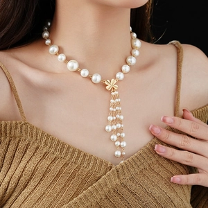 Macro shot of faux pearl necklace with gold clover pendant and long tassel on a model