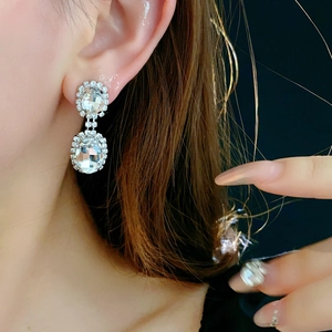 Macro shot of French style silver oval earrings with sparkling diamonds on a model