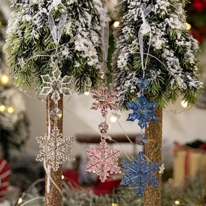 Close-up of clear, pink, and blue acrylic snowflake ornaments hanging on a pine tree branch
