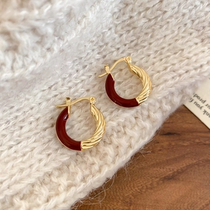 Detail of gold twisted hoop earrings with burgundy enamel on a knit texture background
