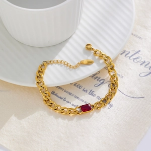 Close-up of golden Cuban link bracelet with red rectangular zircon on vintage paper
