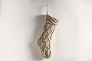 Detailed view of beige knit Christmas stocking with classic cable knit pattern on white wall