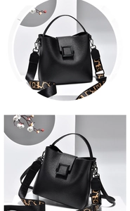 Detail view of a black bucket bag with a brown patterned wide shoulder strap and square buckle