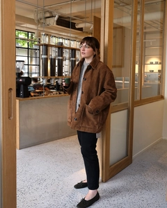 Veste vintage en daim marron portée avec un pull gris dans un café bien éclairé