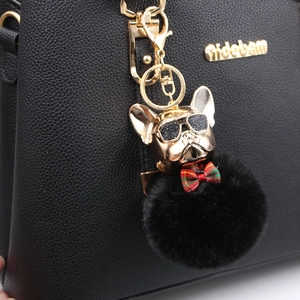 Portachiavi bulldog francese dorato con occhiali e pompon nero su una borsa